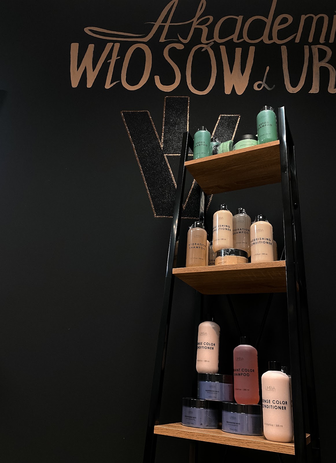 Grafitowa ściana salonu z miedzianym napisem Akademia Włosów i Urody oraz półką z kosmetykami